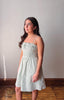 Woman wearing a light green dress standing against a plain wall.