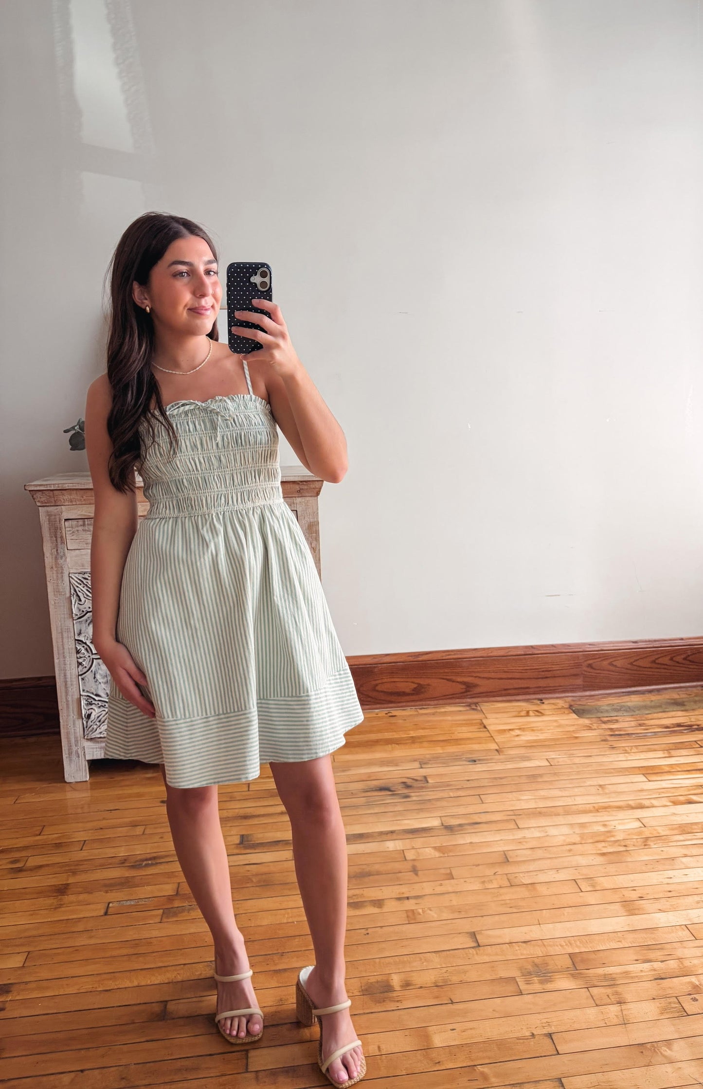 Woman taking a mirror selfie wearing a light green dress in a room with wooden flooring.