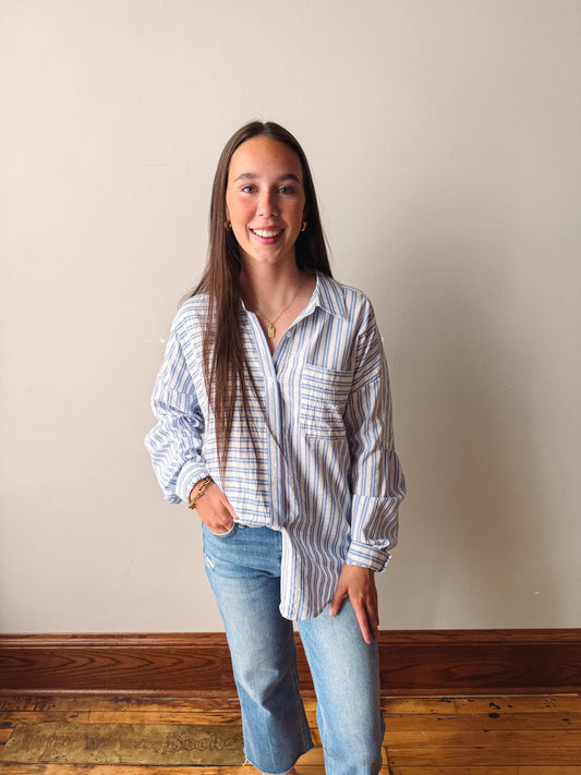 Woman wearing a striped shirt and jeans standing against a plain wall.