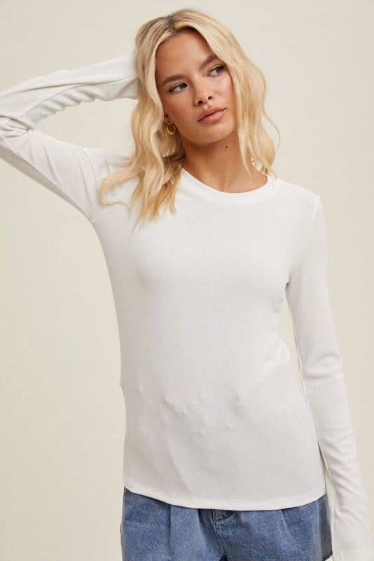 Woman wearing a white long-sleeve top and blue jeans against a plain background