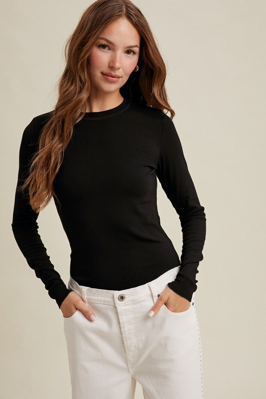 Woman wearing a black long-sleeve top and white pants on a beige background