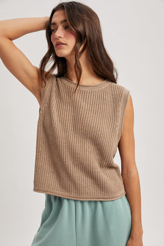 Woman wearing a beige sleeveless knitted top against a plain background