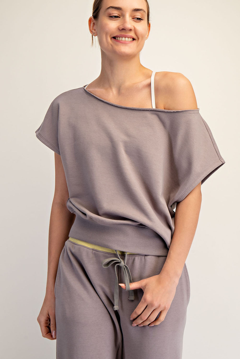Woman wearing a gray off-shoulder top and pants on a plain background