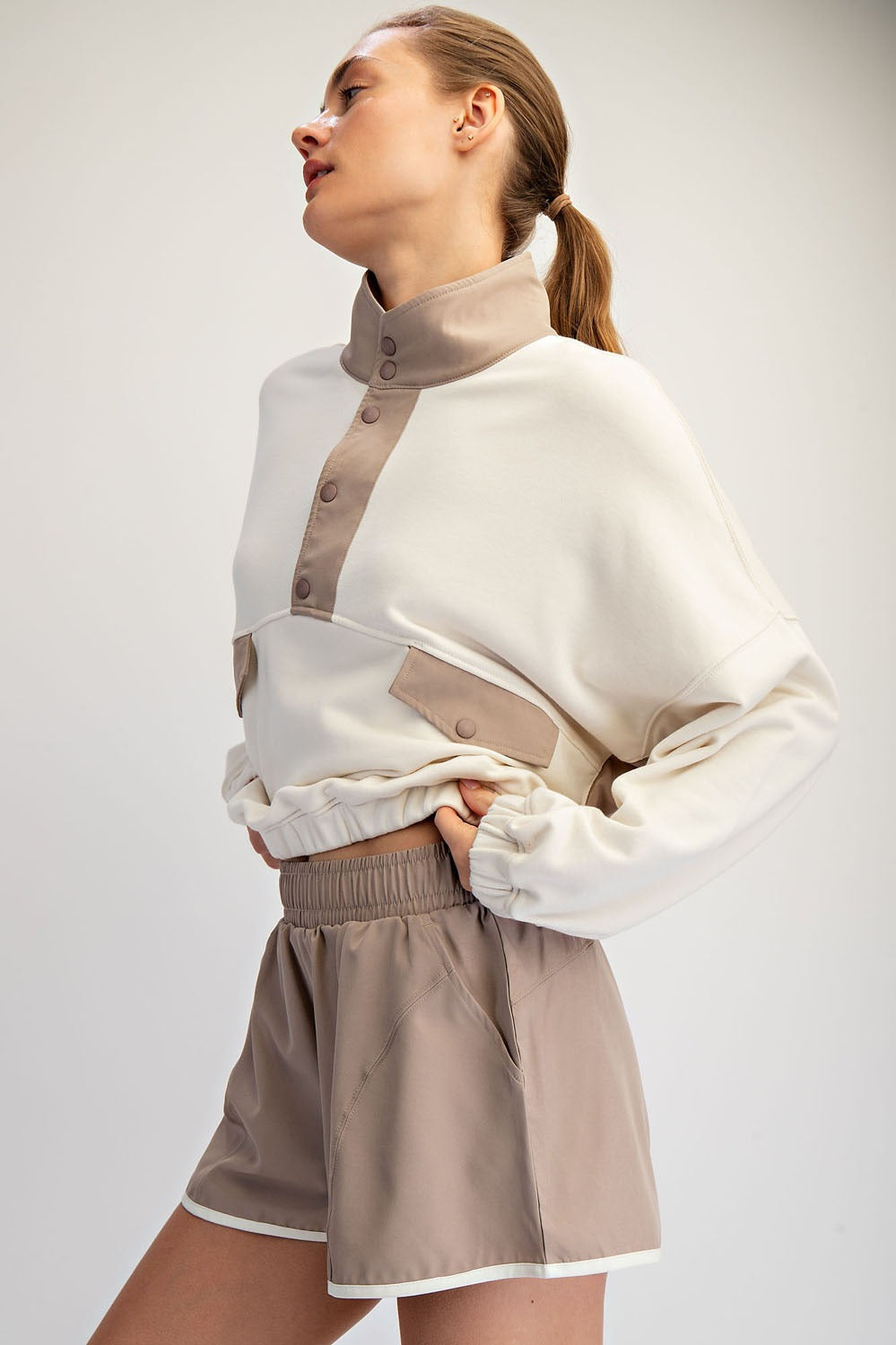 Woman wearing a white sweater with beige accents and matching shorts on a plain background