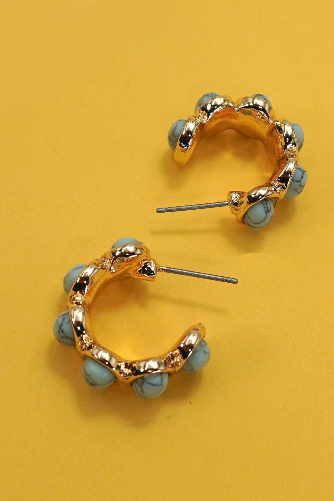 Gold hoop earrings with blue beads on a yellow background