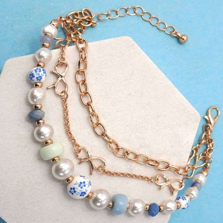 Two layered bracelets with pearls and floral beads on a white stand against a blue background