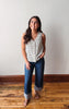 Woman wearing a striped tank top and jeans standing on a wooden floor with a white wall background