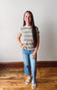 Woman wearing a striped shirt and jeans standing on a wooden floor with a white wall background