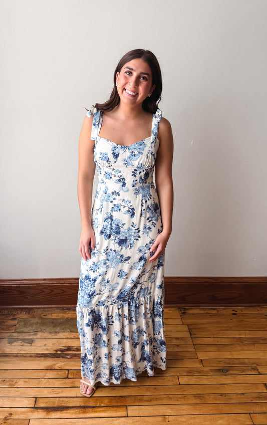 Woman wearing a floral dress standing on a wooden floor with a white wall background