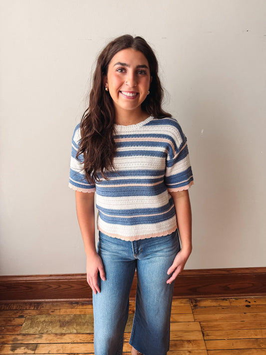 Woman wearing a blue and white striped shirt and jeans standing against a plain wall.