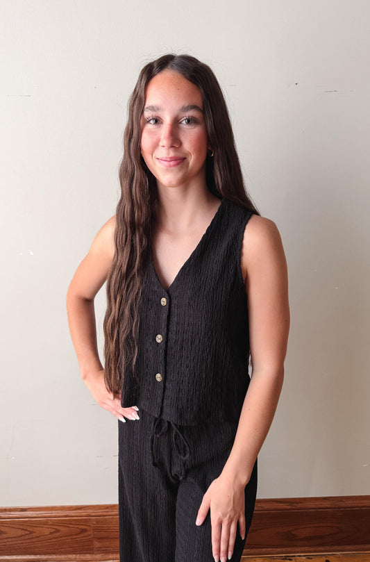 Woman wearing a black sleeveless top with buttons against a plain background