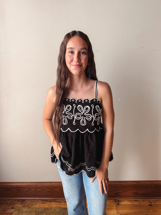 Woman wearing a black top with white patterns against a plain wall.