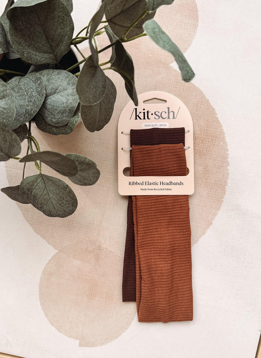 A package of Kit-Sch ribbed elastic headbands in rust brown and dark brown, displayed on a neutral beige background with decorative green leaves.