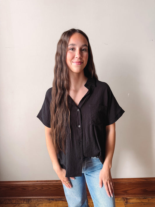 Woman wearing a black blouse and blue jeans against a plain wall.