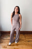 Woman wearing a gray sleeveless top and wide-leg pants standing on a wooden floor.