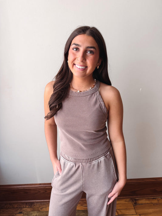Woman wearing a matching beige sleeveless top and pants set against a plain wall.
