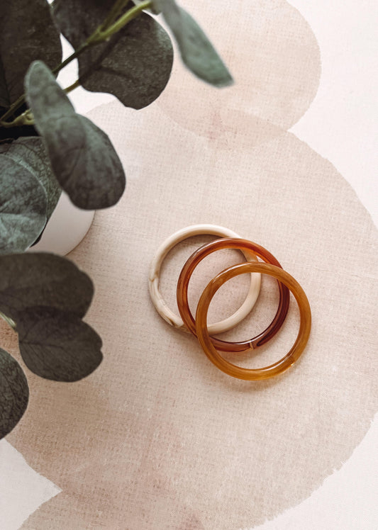 Three tortoiseshell bangles on a textured surface with green leaves in the corner.