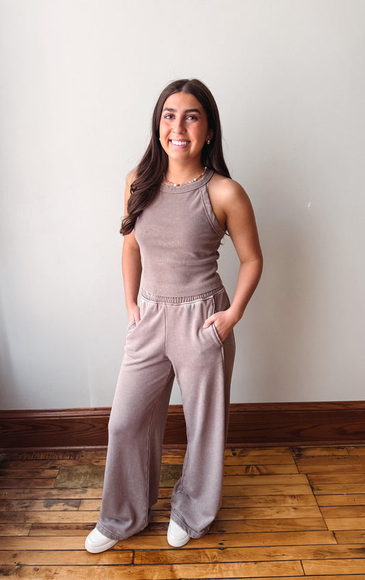 Woman wearing a matching tank top and pants set standing on a wooden floor against a white wall.