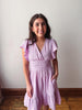 Woman wearing a light purple dress against a plain wall.