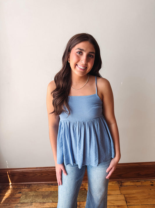 Woman wearing a light blue top and jeans standing against a plain wall.