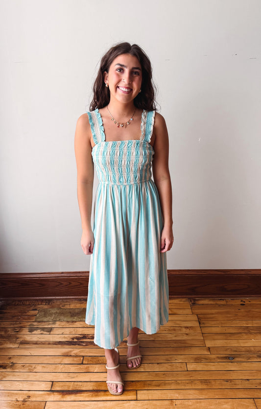 Woman wearing a light blue striped dress standing on a wooden floor with a white wall background