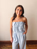 Woman wearing a light blue strapless jumpsuit standing against a plain wall.