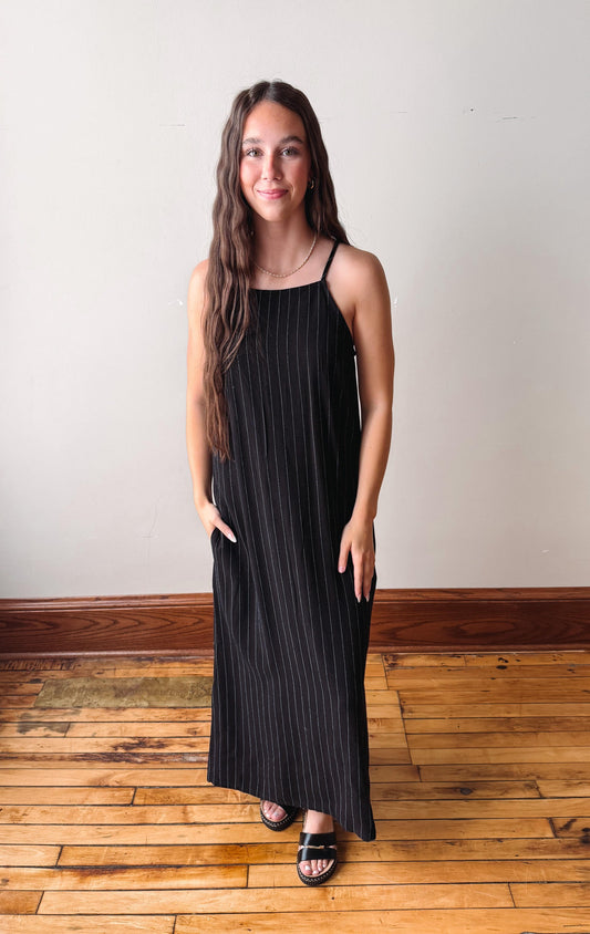 Woman wearing a black dress standing on a wooden floor with a white wall background