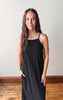 Woman wearing a black pinstripe dress standing against a plain white wall.