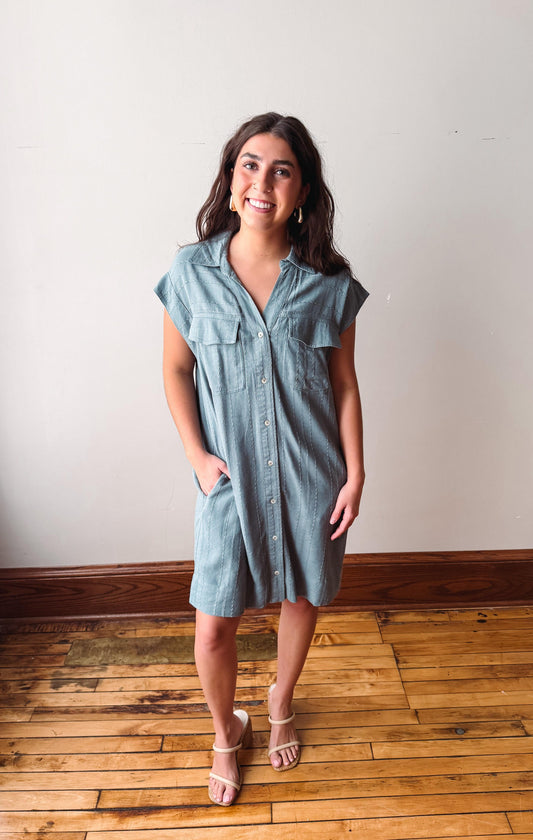 Woman wearing a light blue dress standing on a wooden floor with a white wall background
