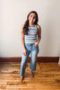 Woman wearing a striped tank top and jeans standing on a wooden floor.