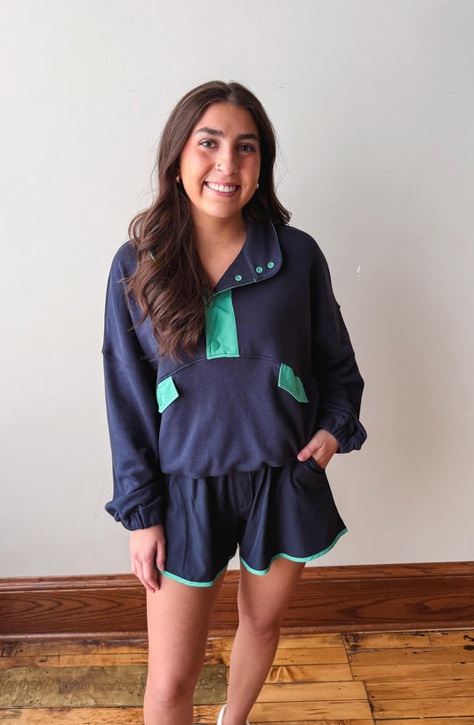 Woman wearing a navy blue outfit with green accents against a plain wall.
