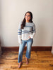 Woman wearing a striped sweater and jeans standing on a wooden floor.