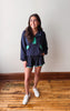 Woman wearing a navy blue outfit with green accents on a wooden floor.
