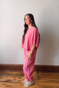 Woman wearing a pink outfit standing against a white wall.