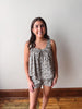 Woman wearing a floral romper against a plain wall.