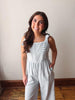 Woman wearing a light gray jumpsuit standing against a plain wall.