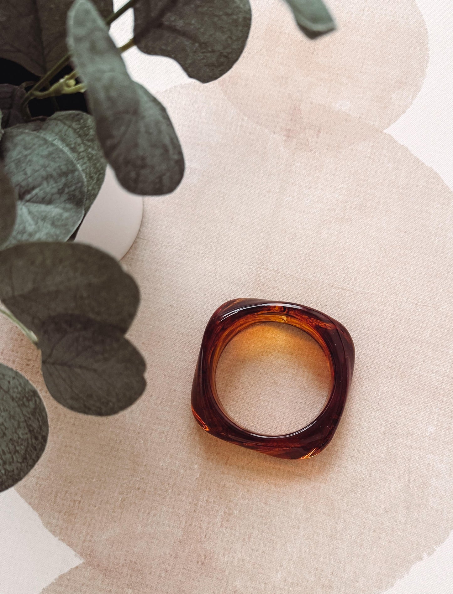 Tortoiseshell ring on a textured beige surface with green leaves.