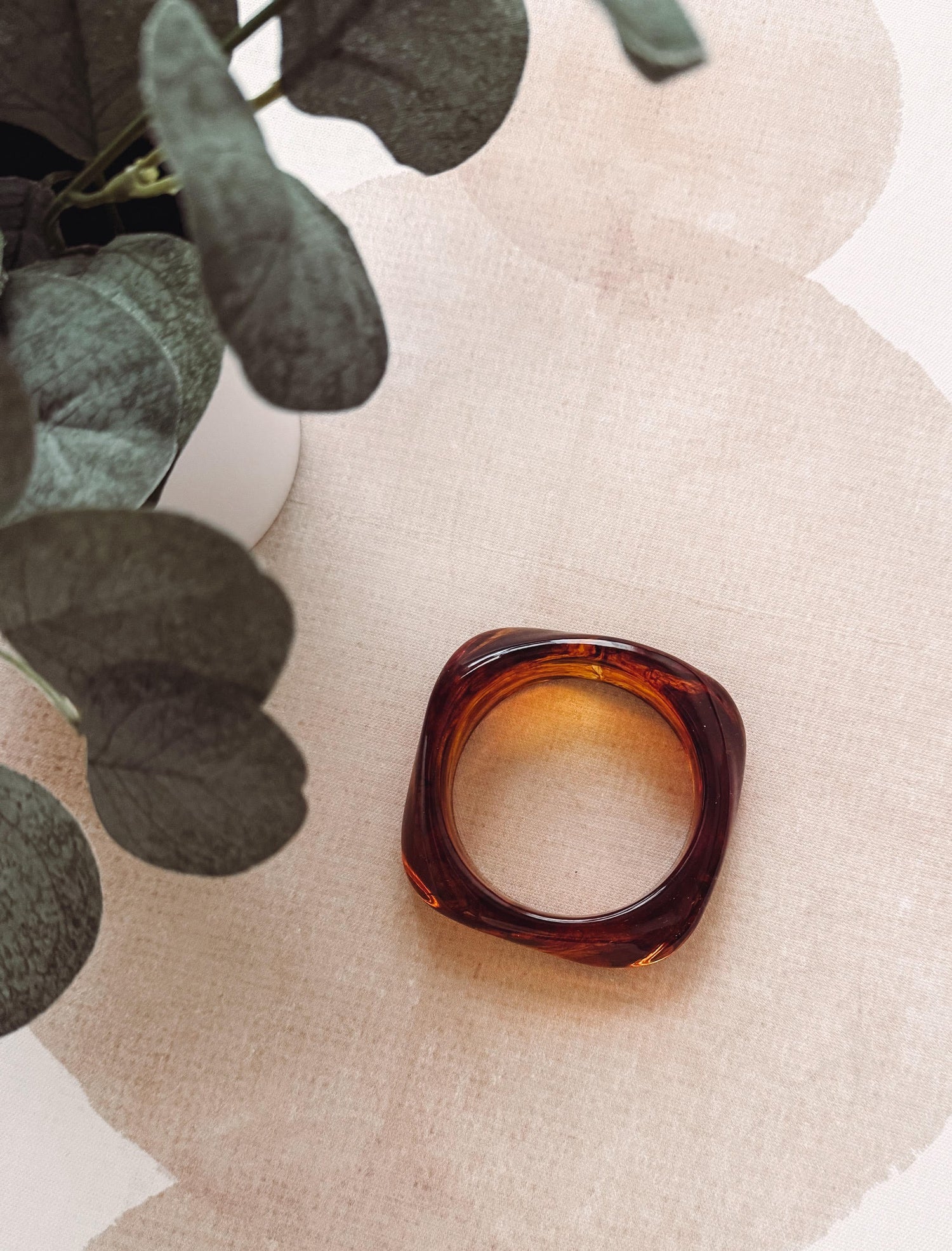 Tortoiseshell ring on a textured beige surface with green leaves.
