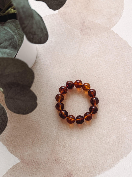 Brown beaded bracelet on a textured beige surface with green leaves.