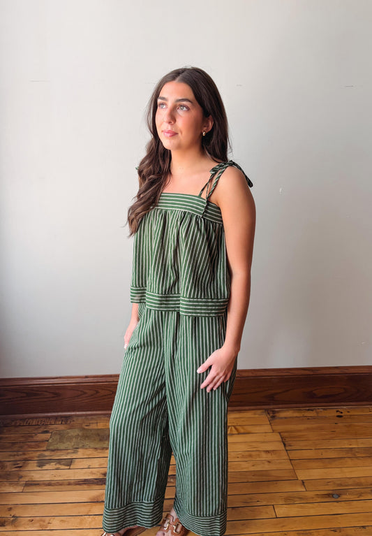 Woman wearing a green striped jumpsuit standing on a wooden floor with a white wall background