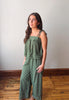 Woman wearing a green striped jumpsuit standing on a wooden floor with a white wall background