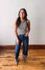 Woman wearing a striped tank top and jeans standing on a wooden floor with a white wall background