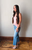 Woman wearing a pink top and blue jeans standing against a plain wall.