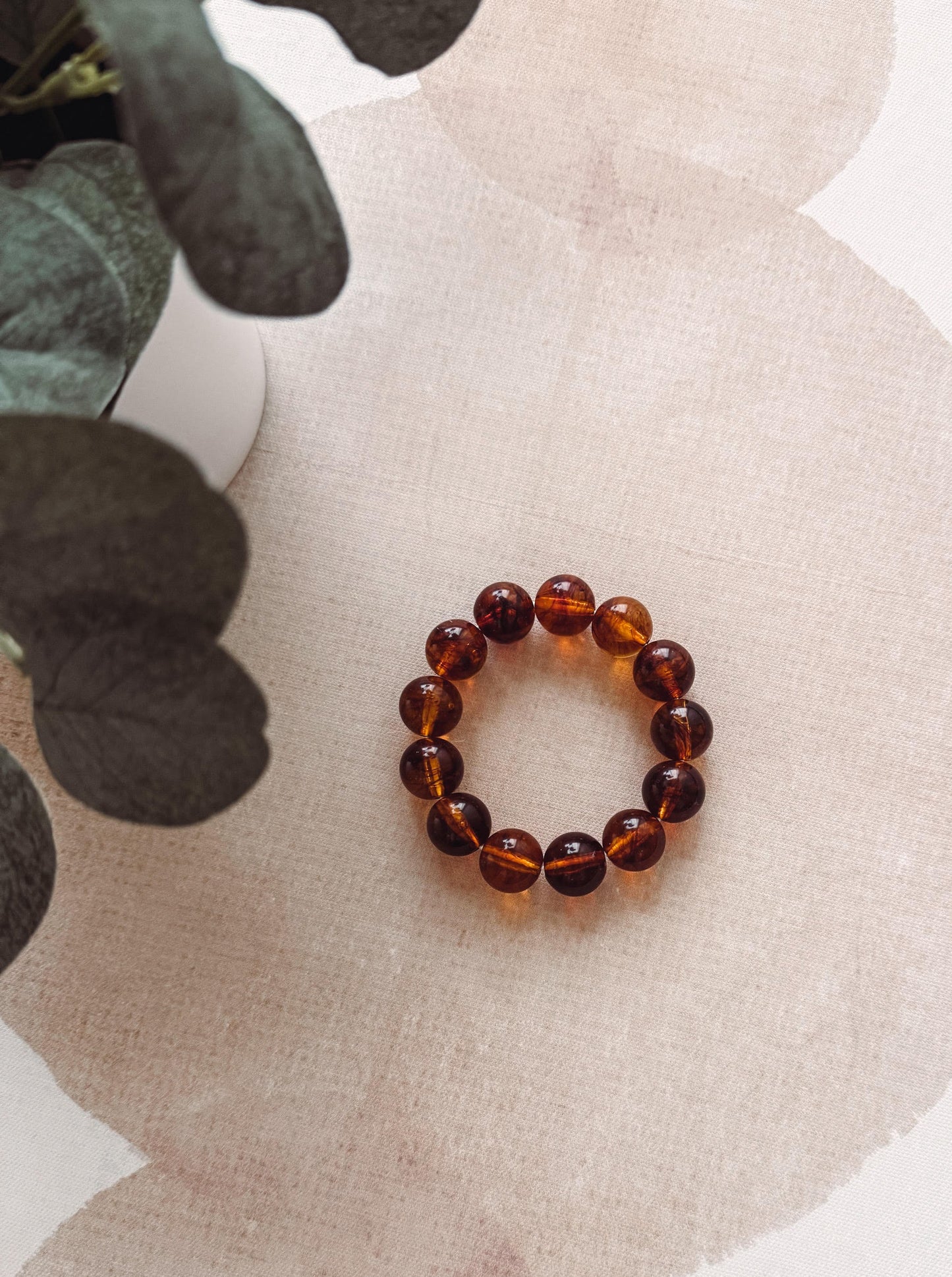 Brown beaded bracelet on a textured beige surface with green leaves.
