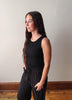 Woman wearing a black sleeveless top and black pants against a plain wall.