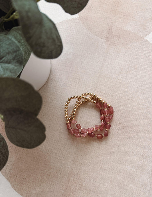 Stack of pink beaded bracelets on a textured surface with greenery in the background