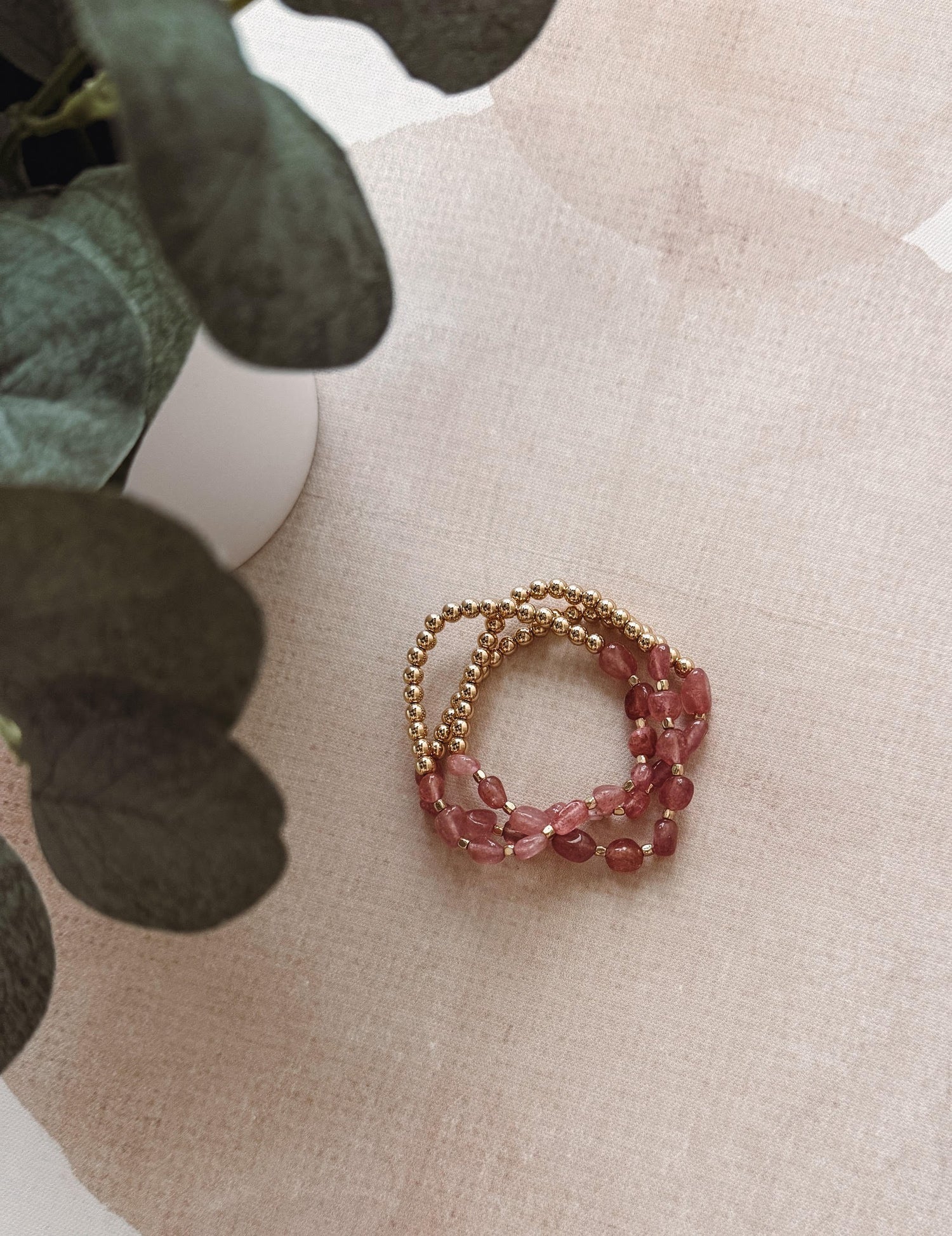 Stack of pink beaded bracelets on a textured surface with greenery in the background