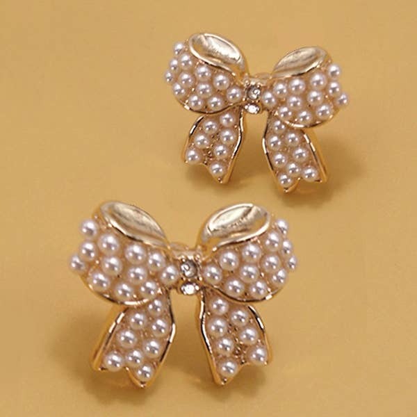 Bow-shaped earrings with pearl details on a beige background