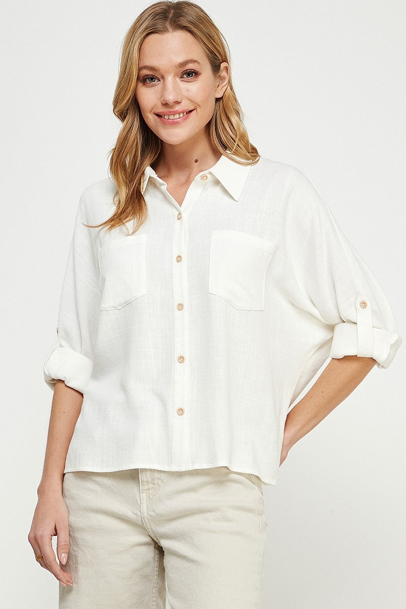 Woman wearing a white button-up shirt and beige pants against a plain background