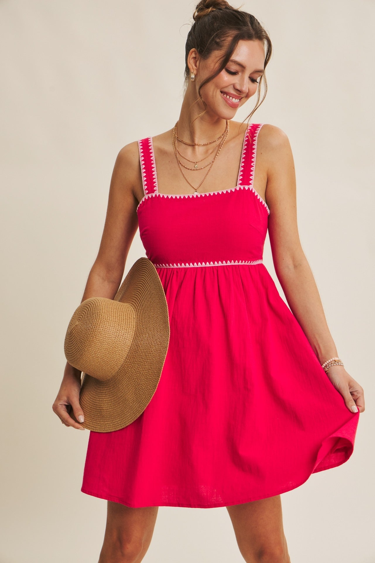 Woman wearing a red dress with white trim, holding a straw hat against a beige background